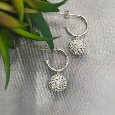 A pair of sterling silver hoop earrings with disco ball drops, displayed on a textured surface with greenery in the background.