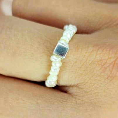 A tiny freshwater pearl ring with an elastic band, displayed on a person's finger.