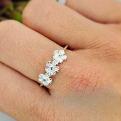 A hand holding a sterling silver ring with three flower-shaped embellishments on it.