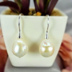 A pair of sterling silver drop earrings with pearls displayed in front of a potted plant.