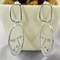 A pair of sterling silver long statement face drop earrings displayed in front of a potted plant.
