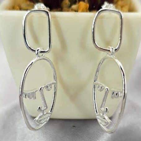A pair of sterling silver long statement face drop earrings displayed in front of a potted plant.