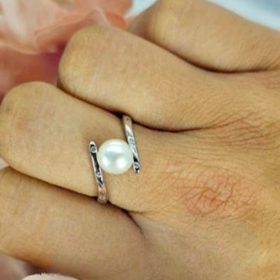 A hand holding a sterling silver ring with a freshwater pearl, with an adjustable clasping mechanism.
