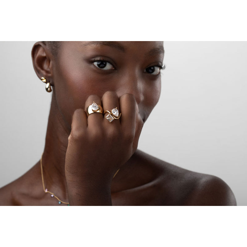 Woman wearing gold earrings, rings, and a necklace on a plain background