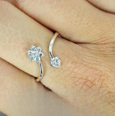 An adjustable sterling silver ring with cubic zirconia in the shape of a heart and flower ends, displayed on a person's hand.