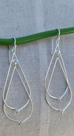 Silver teardrop earrings hanging on a green wire against a gray background