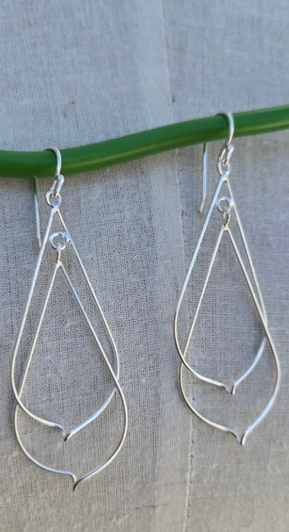Silver teardrop earrings hanging on a green wire against a gray background