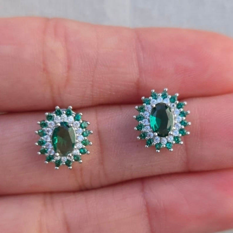 Pair of green gemstone earrings held between fingers against a neutral background