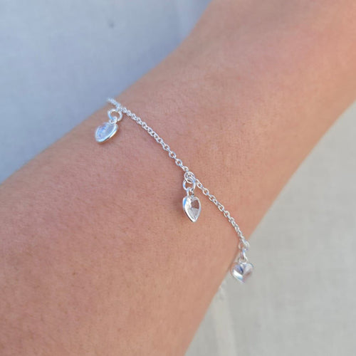 Silver bracelet with heart-shaped charms on a wrist against a light background