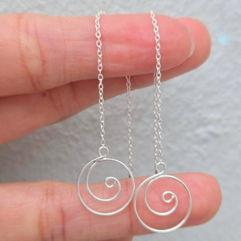Silver spiral pendant necklace held between fingers against a neutral background