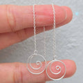 Silver spiral pendant necklace held between fingers against a neutral background
