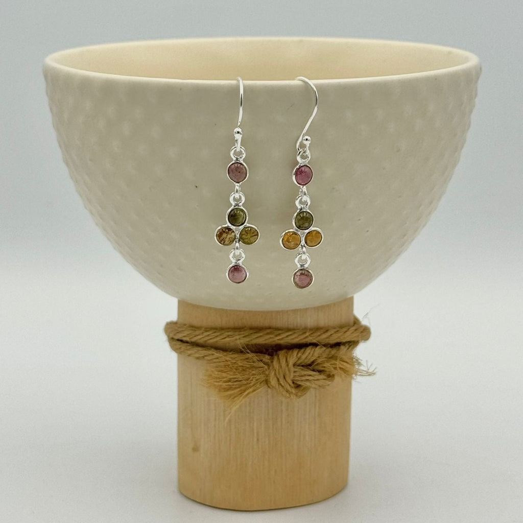 Pair of earrings with colored beads displayed in a ceramic bowl on a white background