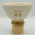 Pair of earrings with colored beads displayed in a ceramic bowl on a white background