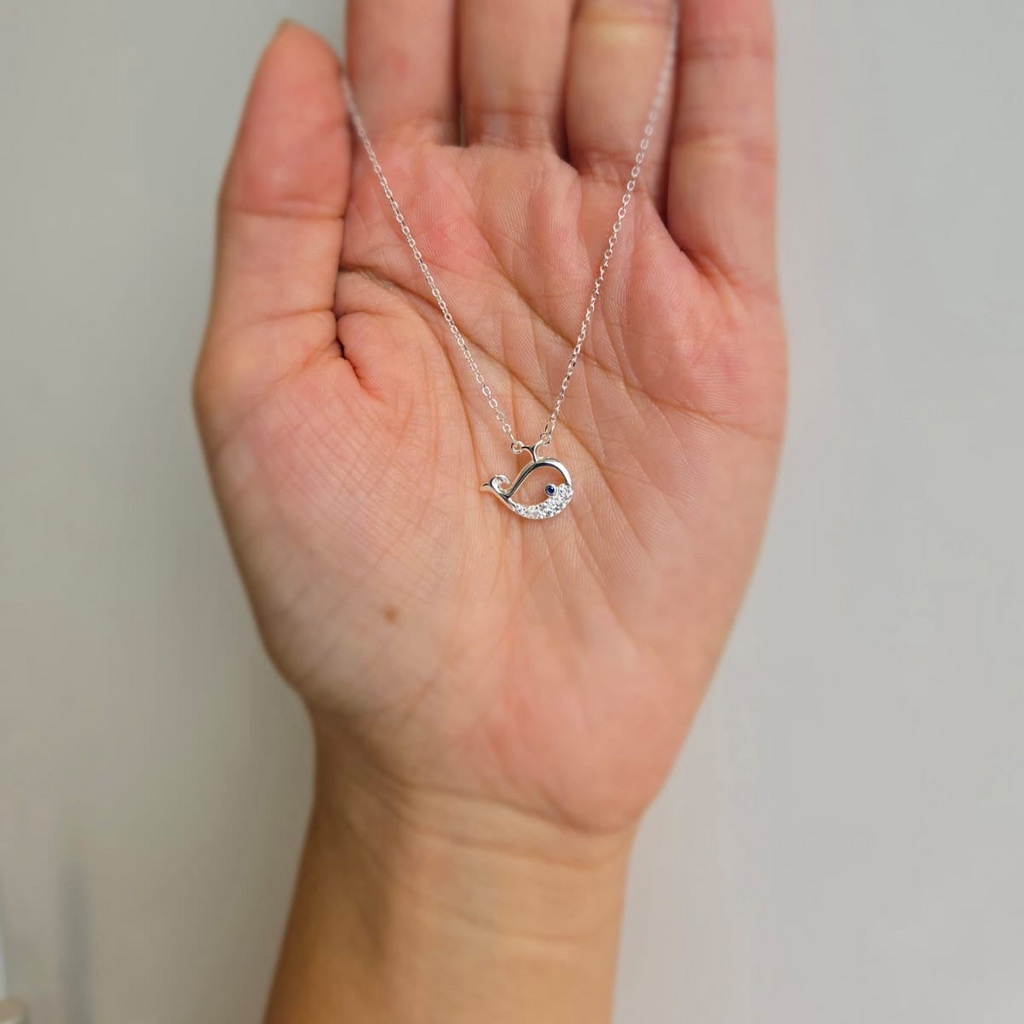 A hand holding a sterling silver necklace with a cubic zirconia encrusted dolphin charm.