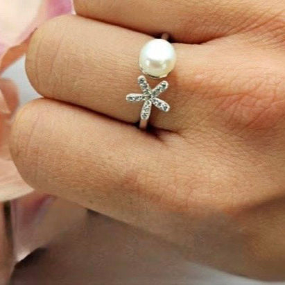 A sterling silver ring with a freshwater pearl center and floral accents, worn on a person's finger.