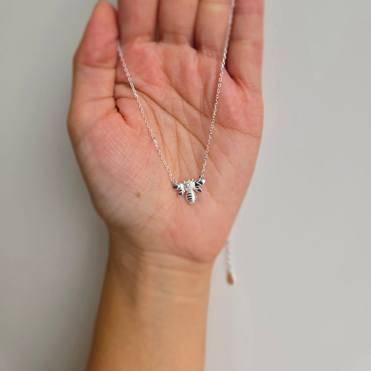 A hand holding a sterling silver necklace with a small bee charm.