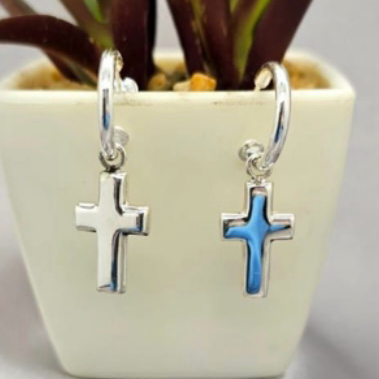 A pair of sterling silver cross earrings with blue enamel detailing, displayed in front of a potted plant.