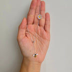 A sterling silver V shape necklace with a daisy flower and bee design, held in a person's hand.