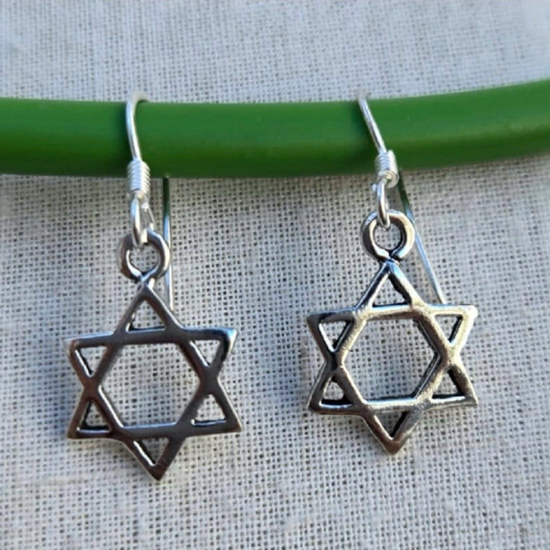 Star-shaped silver earrings on a green stick against a textured fabric background