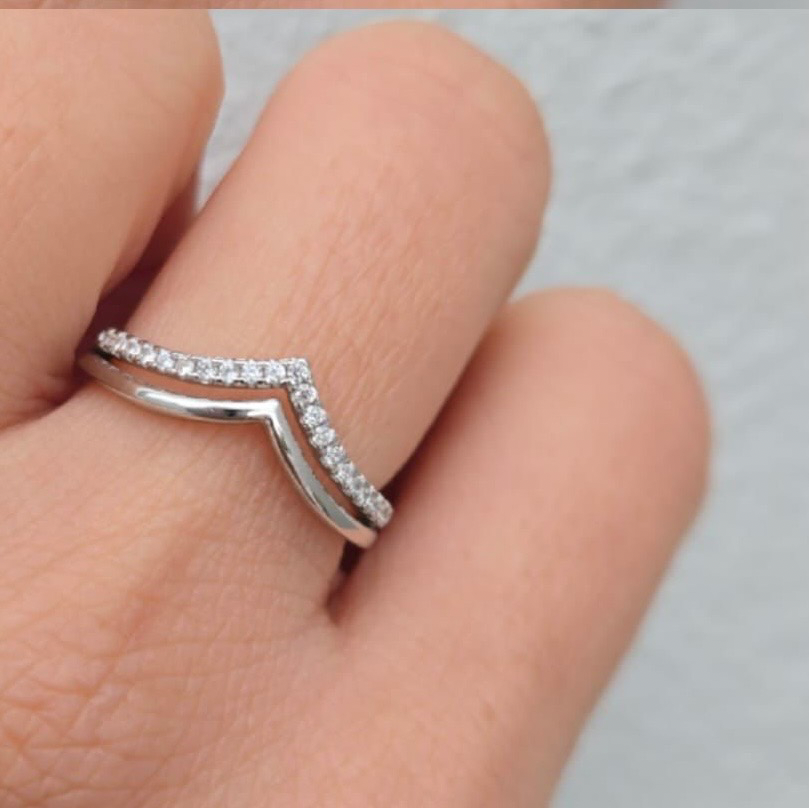 Silver ring with a chevron design on a finger against a neutral background