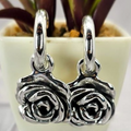The image shows a pair of sterling silver hoop earrings with rose charms, displayed on a table next to a small potted plant.