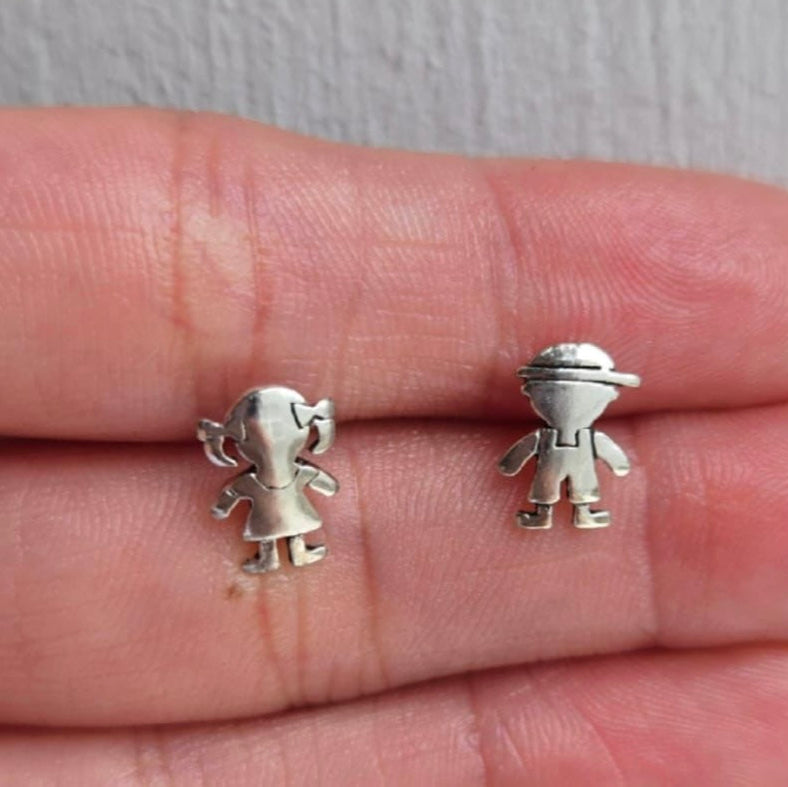 Small silver figurine earrings held between fingers on a neutral background