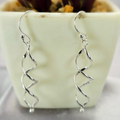 A pair of sterling silver drop earrings with a geometric spiral design, displayed in a white vase with a green plant in the background.