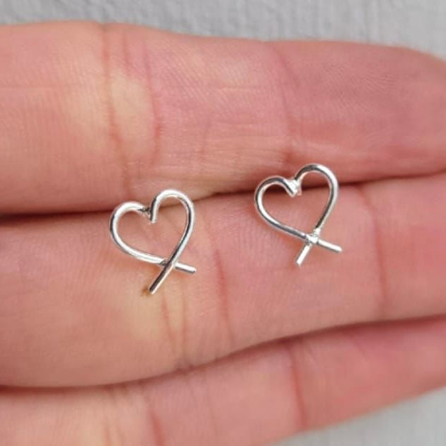 Silver heart-shaped earrings held between fingers on a neutral background