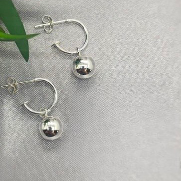 A pair of sterling silver ball earrings with a reflective surface, displayed on a table with a white fabric background.