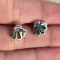 Silver leaf-shaped earrings on a person's finger