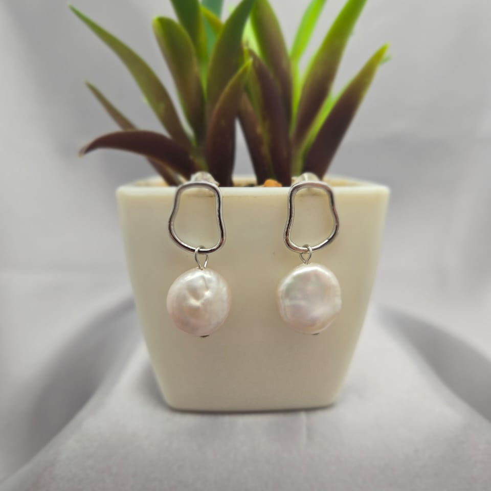 Pearl earrings displayed in front of a small potted plant on a gray background