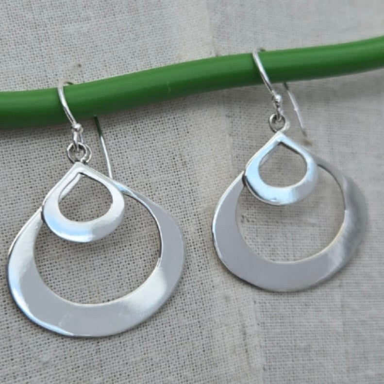Silver hoop earrings hanging on a green stick against a gray background