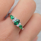 Ring with green gemstones and clear stones on a finger