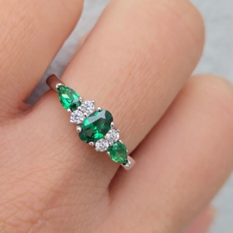 Ring with green gemstones and clear stones on a finger