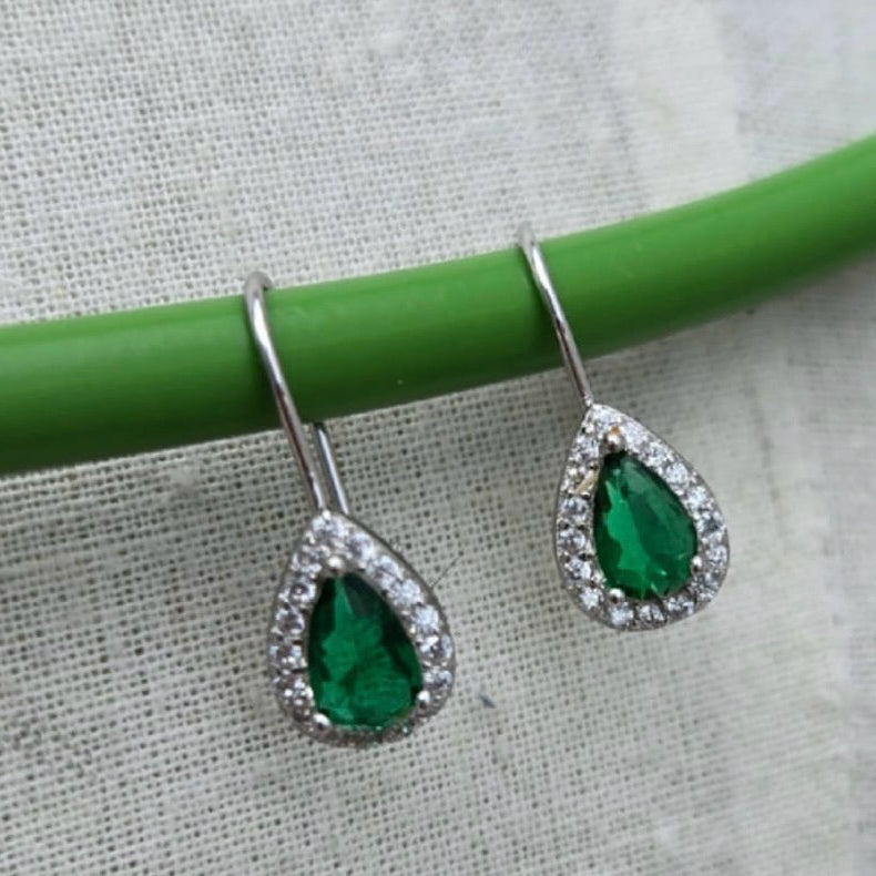 Teardrop-shaped green gemstone earrings on a green stick against a textured white background