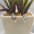 A pair of sterling silver stud earrings designed to resemble leaves, displayed in a white pot with a green plant.
