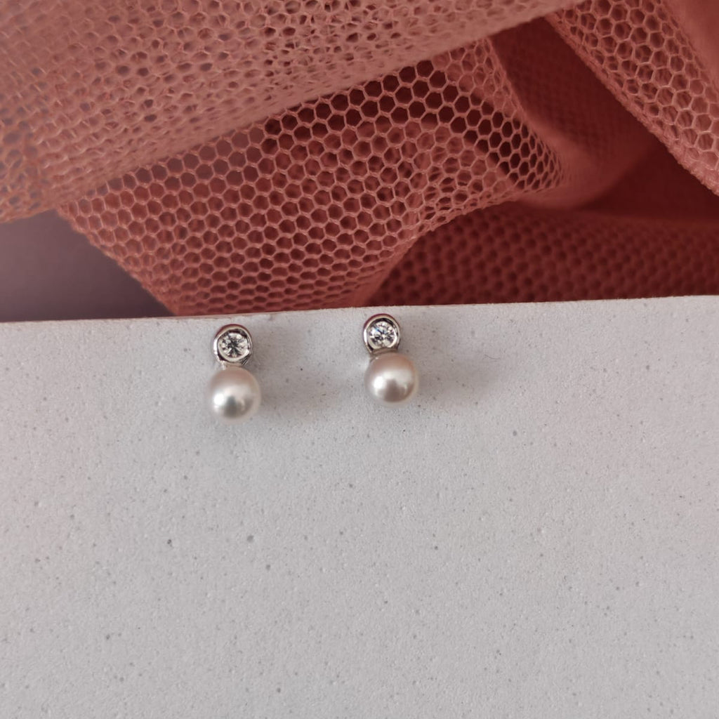 Two silver earrings on a light gray surface with a pink textured fabric in the background.