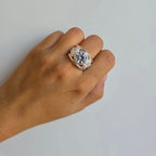 Hand wearing a decorative ring on a plain background