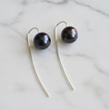 Black pearl earrings on silver hooks against a gray background