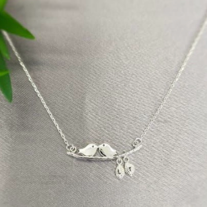 A sterling silver necklace featuring two lovebirds intertwined on a delicate chain, displayed against a grey background.