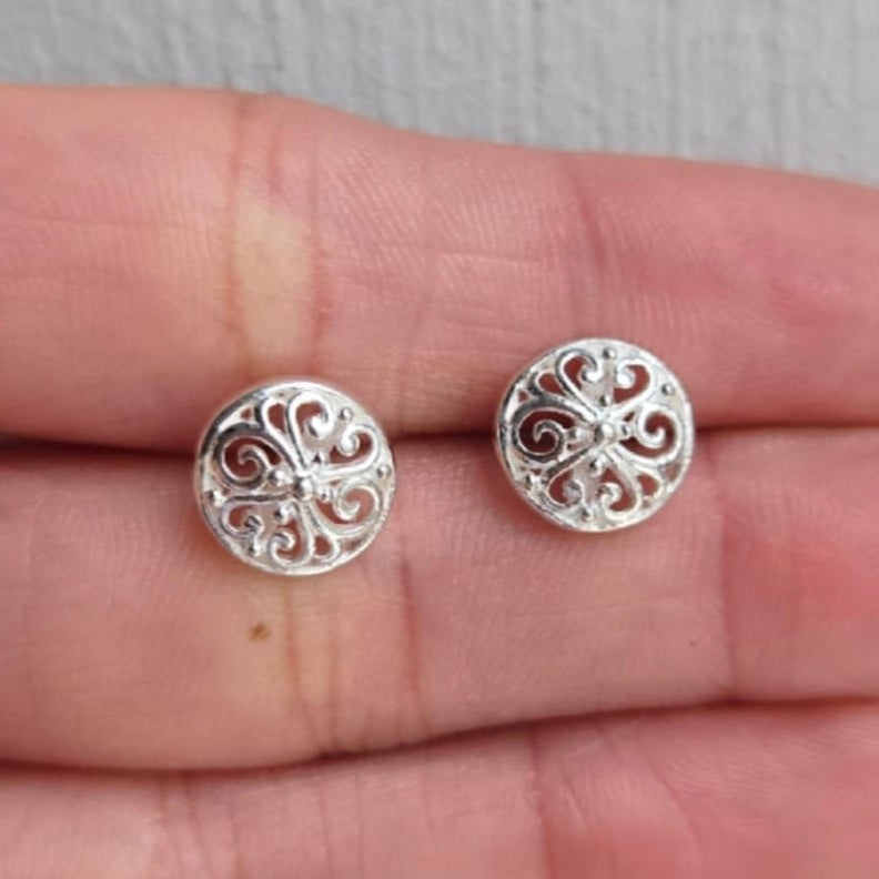 Silver filigree earrings held between fingers on a neutral background