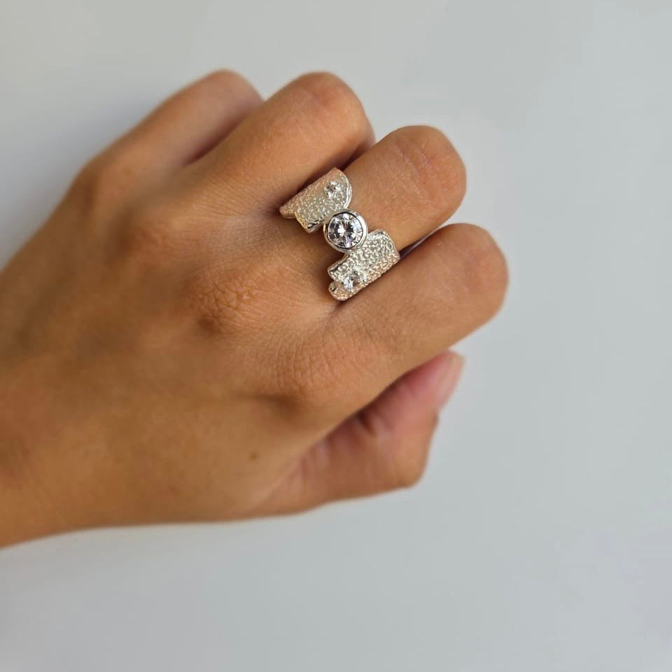 A sterling silver ring with a hammered look and a cubic zirconia center stone, displayed on a person's hand.