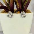 A pair of sterling silver stud earrings with cubic zirconia pave, displayed in a white earring holder with a green plant in the background.