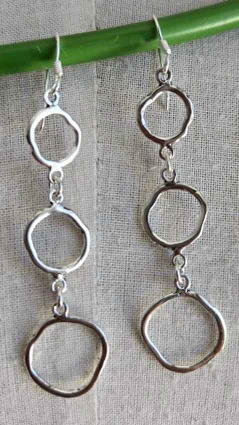 Silver hoop earrings hanging from a green stick on a textured surface
