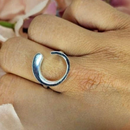 An adjustable sterling silver ring with an open circle detail is displayed on a person's finger.