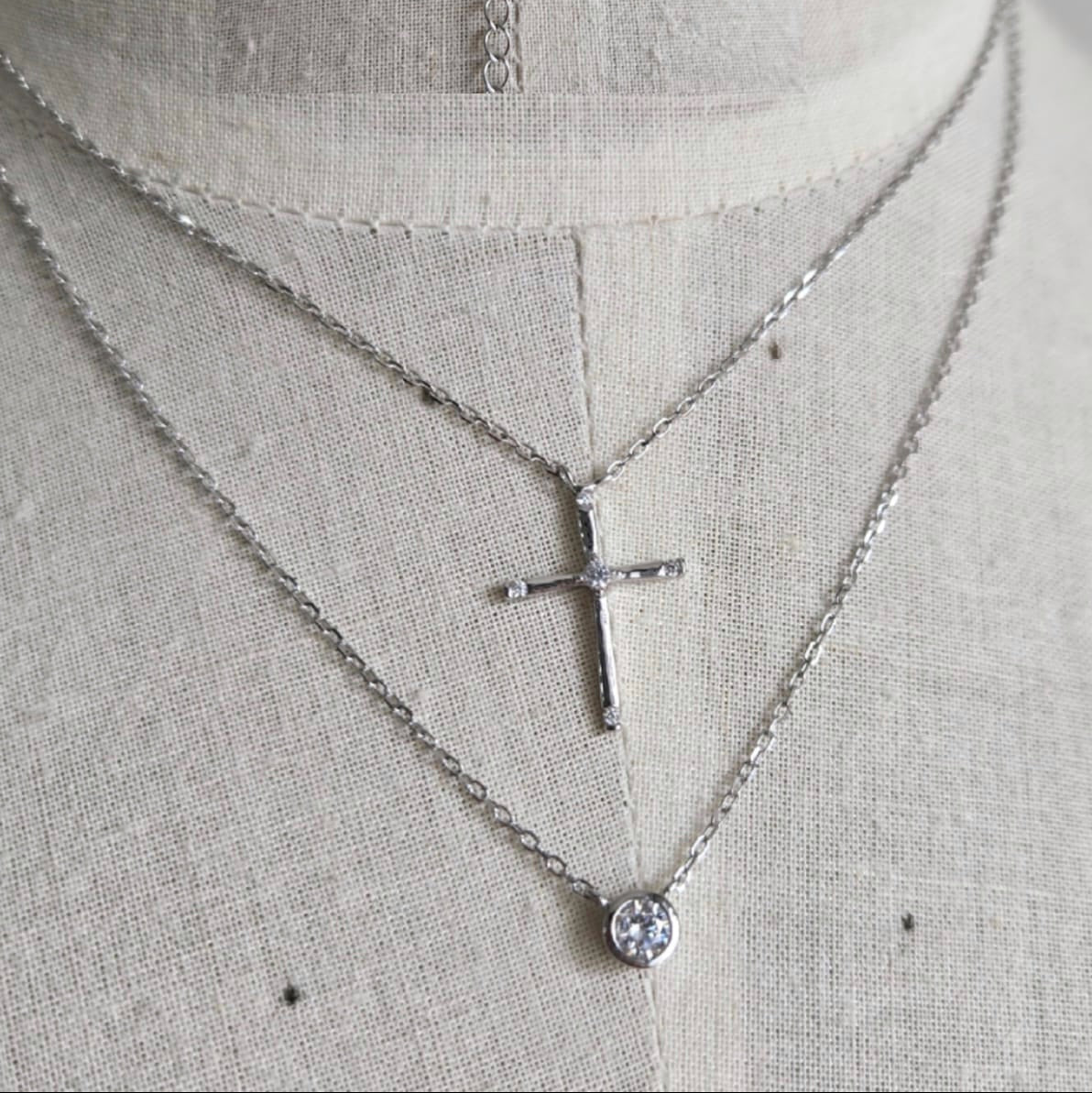 Silver necklace with a cross pendant on a mannequin.