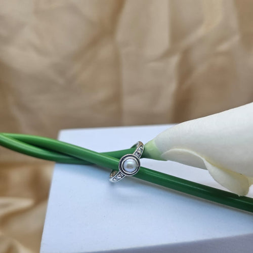 Silver ring with a pearl on a white flower and green stem against a beige background