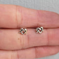 Pair of knot-shaped earrings held between two fingers on a neutral background
