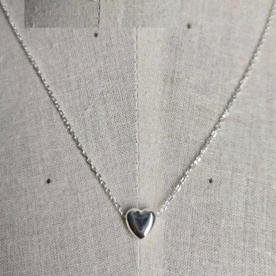Silver heart-shaped pendant necklace on a light gray fabric background