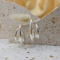 Silver hoop earrings on a textured stone surface with a blurred floral background